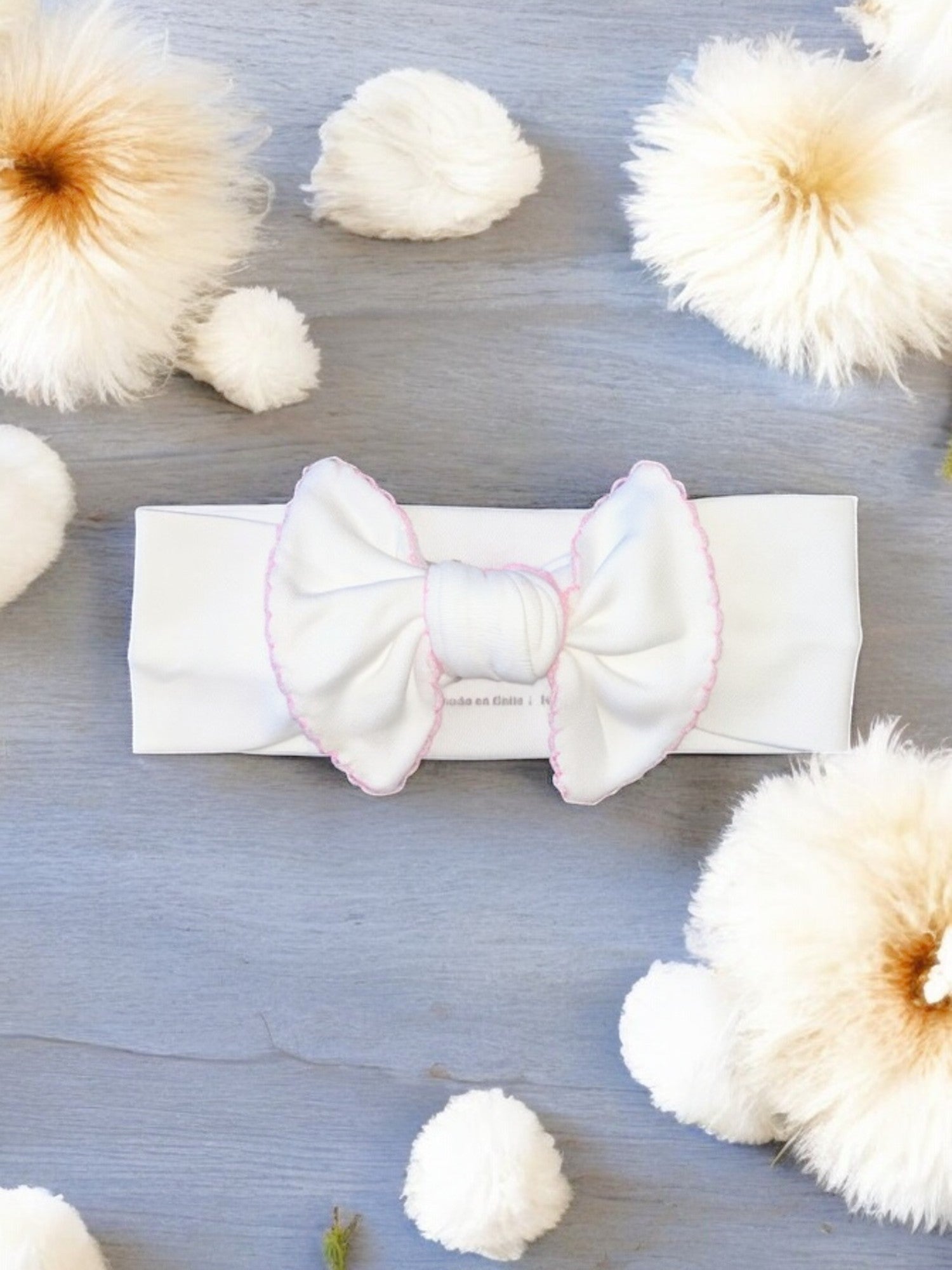 Cintillo rosa para bebé blanco con moño grande y borde rosa sobre fondo gris con decoración de flores